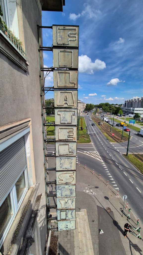 Stary, zabytkowy neon, widać pionowe prostopadłościenne elementy z neonowymi rurkami układającymi się w napis "FILATELISTYKA".